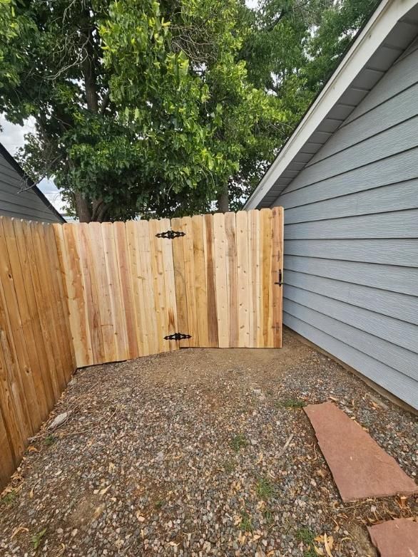 Wooden fence gate between a house and other fence, gravel ground.