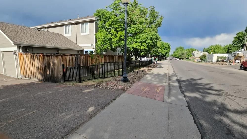 Street with sidewalk, buildings, trees, and cloudy sky. 