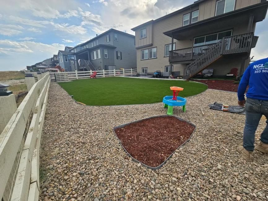Backyard with new artificial turf, gravel, and a small play area. 