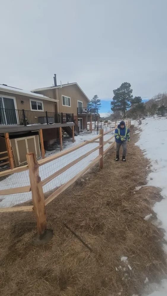 Person standing by a newly built wooden fence near a house, with snow on the ground.