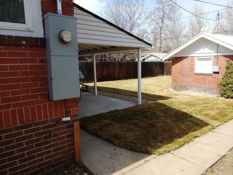 Gray electrical box on red brick building next to carport and lawn with grass.