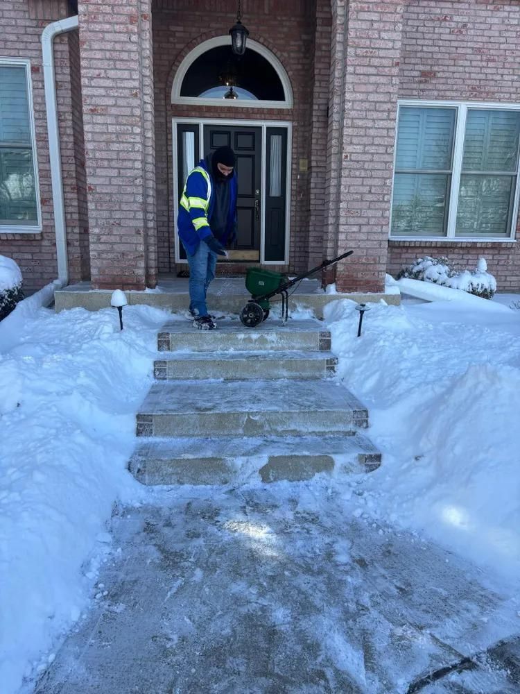Person spreading salt on snowy front steps of a brick house.