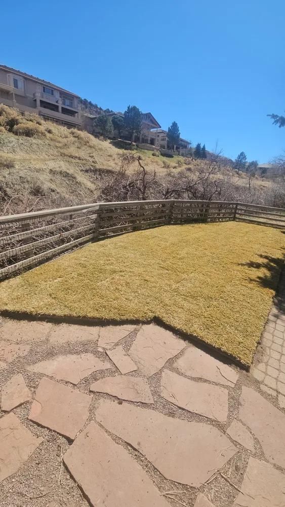 Patio with flagstone pavers, lawn, retaining wall, and hillside houses under a blue sky.