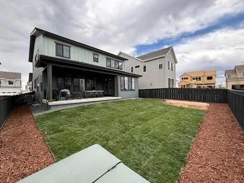 Backyard of a two-story house with green grass, a covered patio, and a wooden fence.