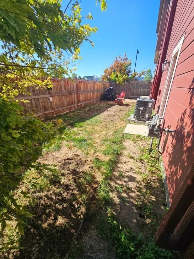 Backyard with a wooden fence, grass, and a red house.