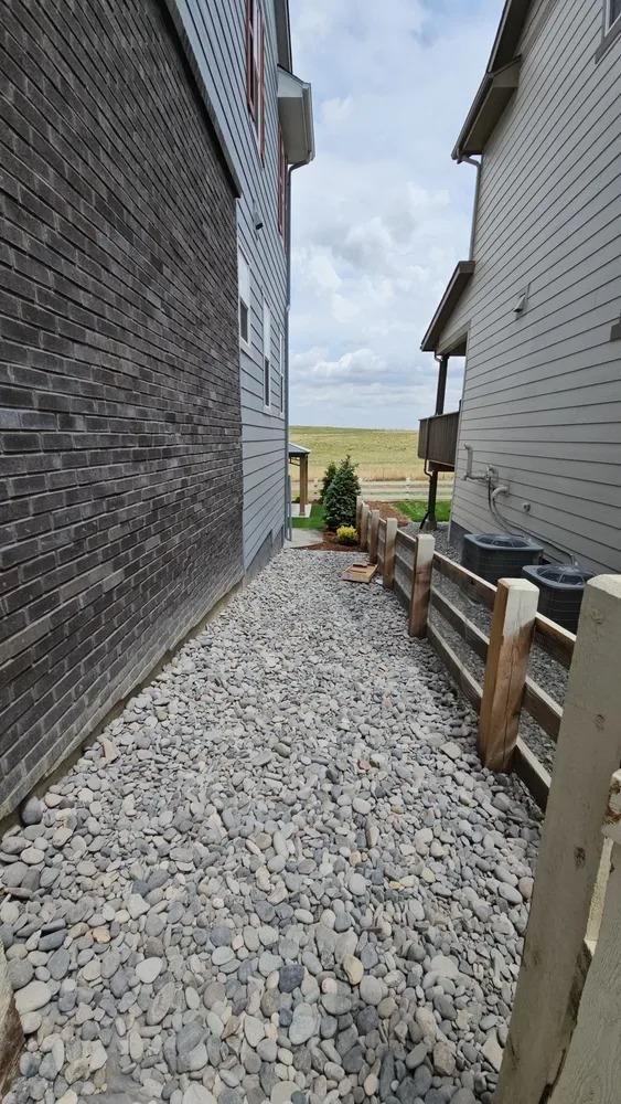 Narrow gravel path between two houses, one with brick, the other with siding and a wooden fence.