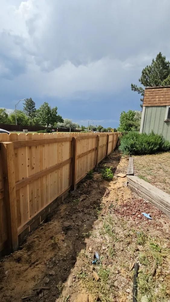 A wooden fence along a yard, under a cloudy sky.