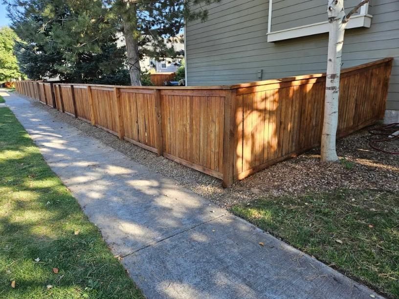 Wooden fence beside a sidewalk and grass, adjacent to a building.