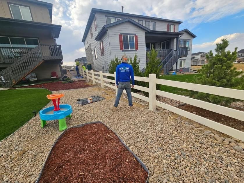 Person standing in front of white fence, house in background. 