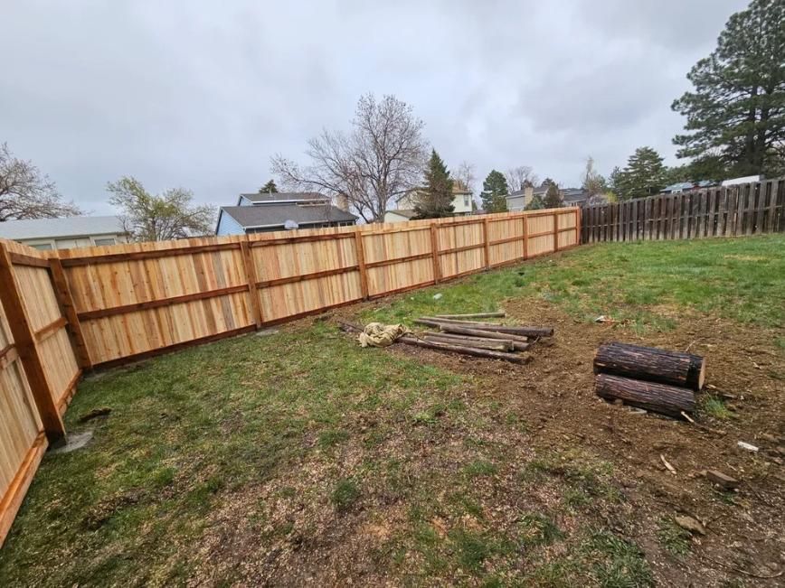 Wooden fence surrounding a grassy backyard on an overcast day. 