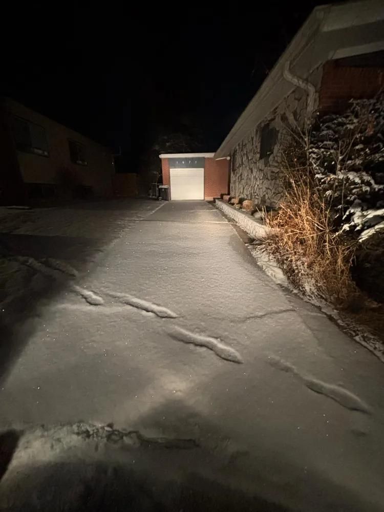 Snow-covered driveway at night leading to an open garage; footprints in the snow.