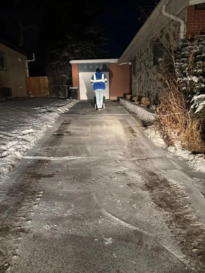 Person in blue vest walks on icy driveway toward a garage at night. 
