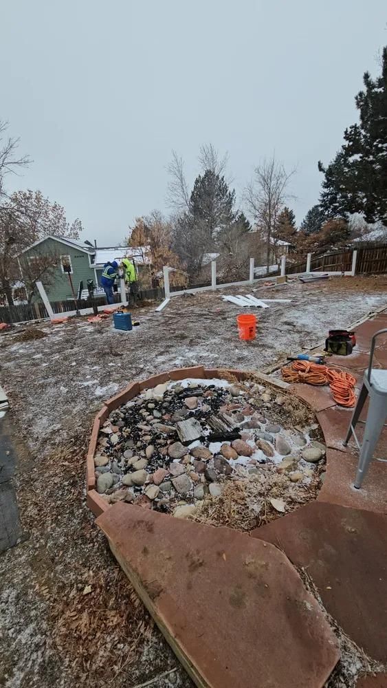 Backyard with a fire pit, patchy snow, and construction workers near a house.