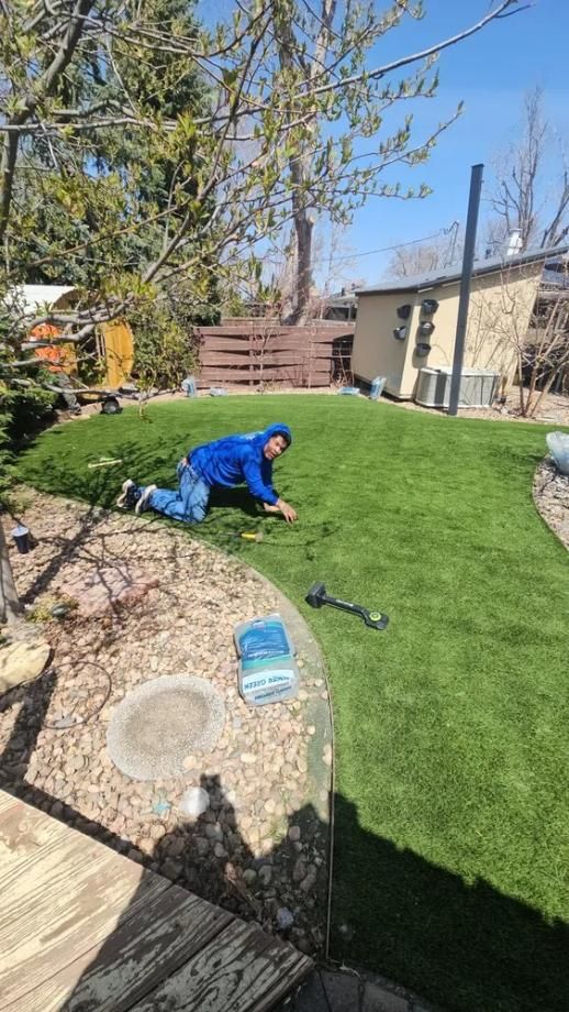 Man in blue jacket works on lawn, sunny day.