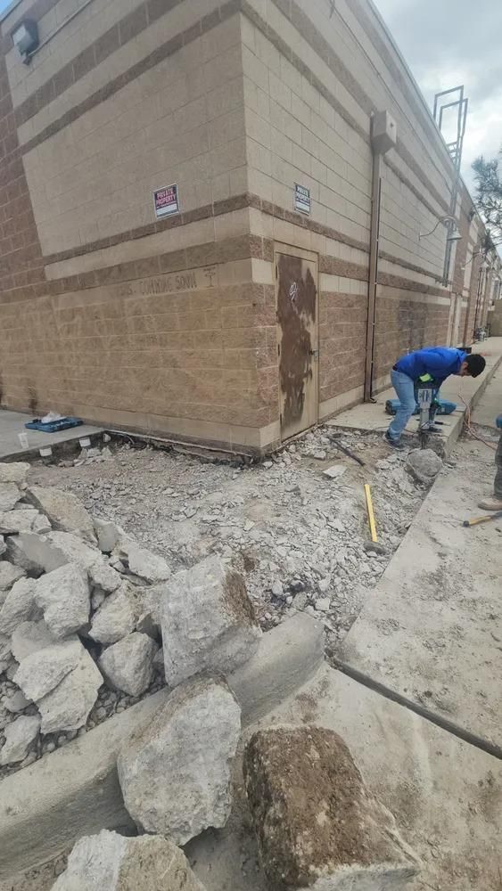 Construction worker using a jackhammer to remove concrete at a building corner. 
