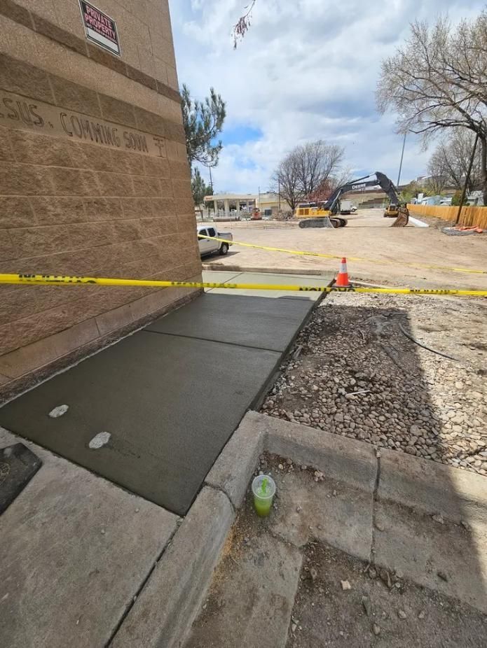 New concrete ramp next to a brick building; construction zone with heavy machinery in the background.