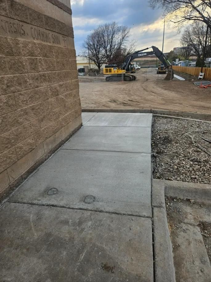 New concrete sidewalk with construction in background, near a brick building.