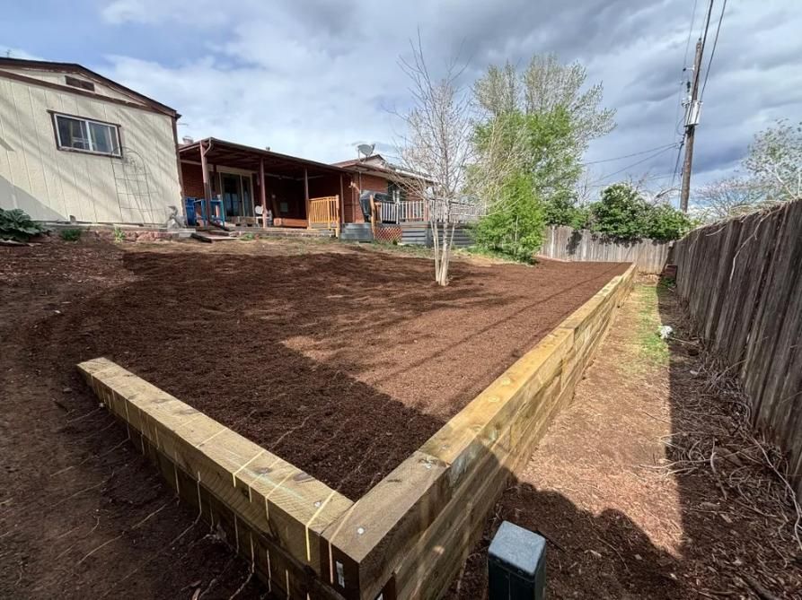 Backyard with raised wooden garden beds filled with mulch, house in background.