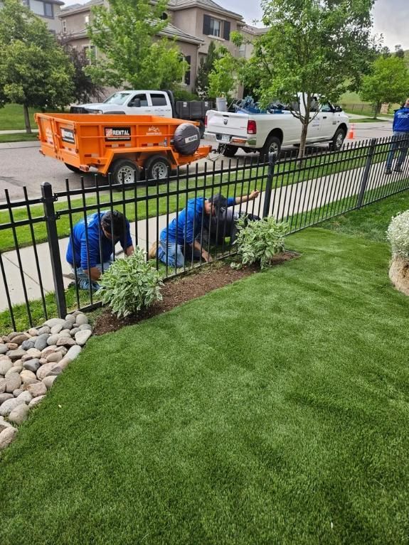 Two people in blue shirts tending to plants behind a black fence. 