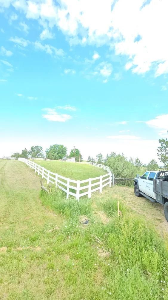 White fence encloses grassy area under a bright blue sky.
