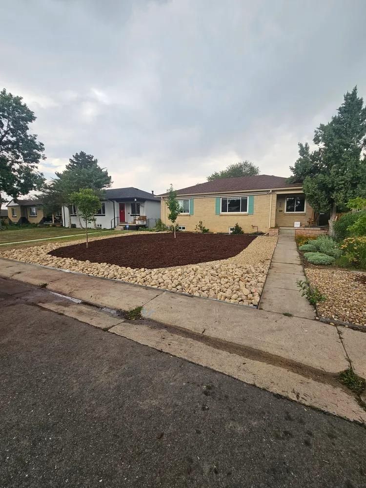 Tan house with turquoise trim and a rock-lined, mulched front yard, viewed from the street.