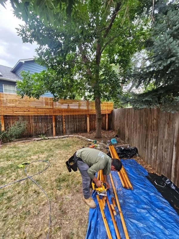Man using a power tool on lumber in a backyard. 