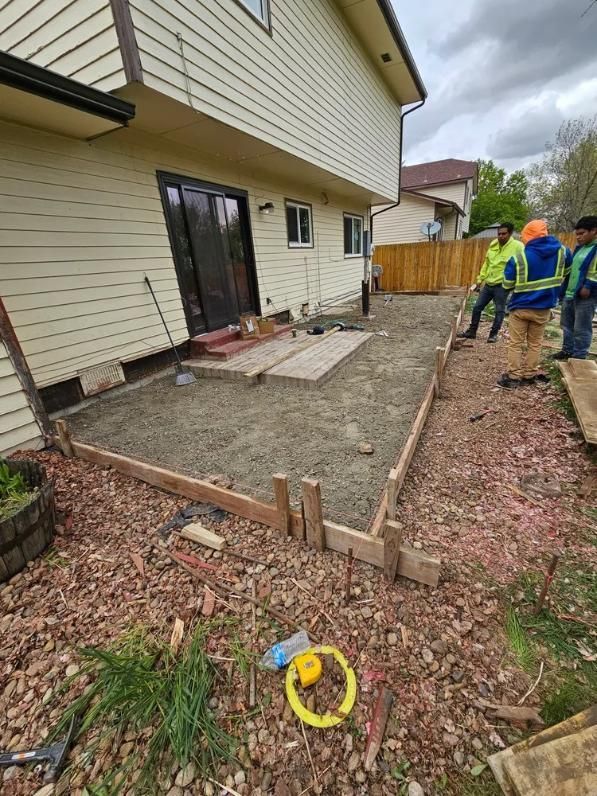 Construction site; workers building concrete patio next to a house. 