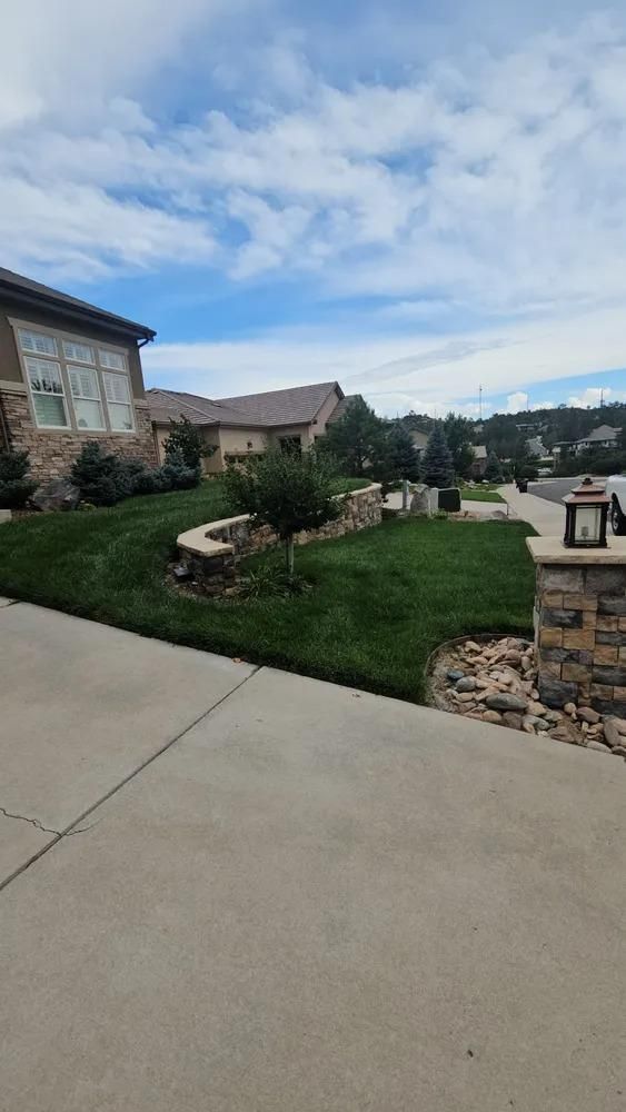 Lush green lawn with a retaining wall in front of a house, under a partly cloudy sky.