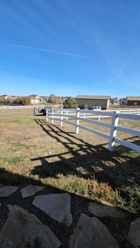 White fence in grassy yard, under a blue sky, with houses in the background.