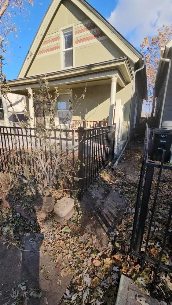 Small house with porch, black fence, and fallen leaves.