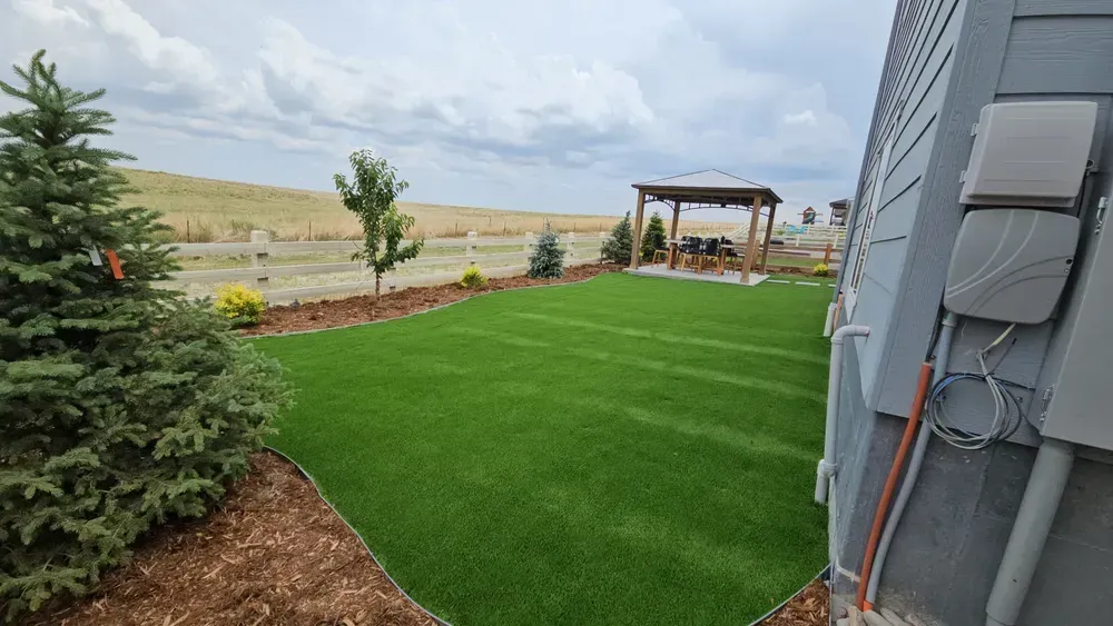 Green turf backyard with gazebo, trees, and cloudy sky.