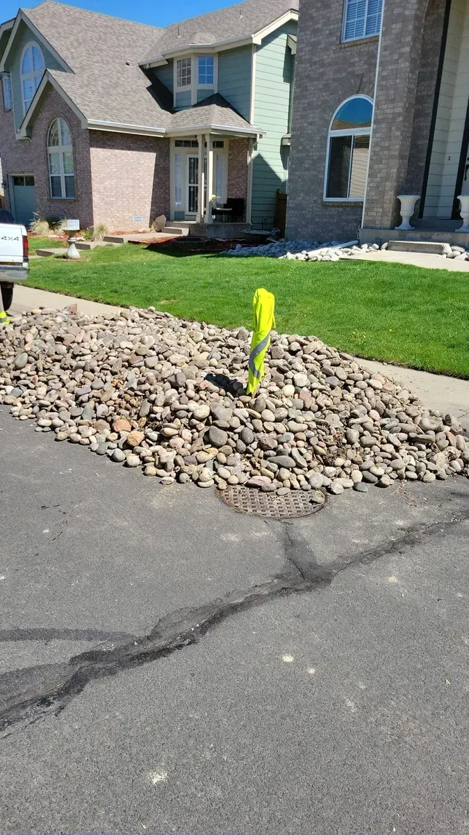 Pile of rocks and yellow marker in front of a house on the side of a road.
