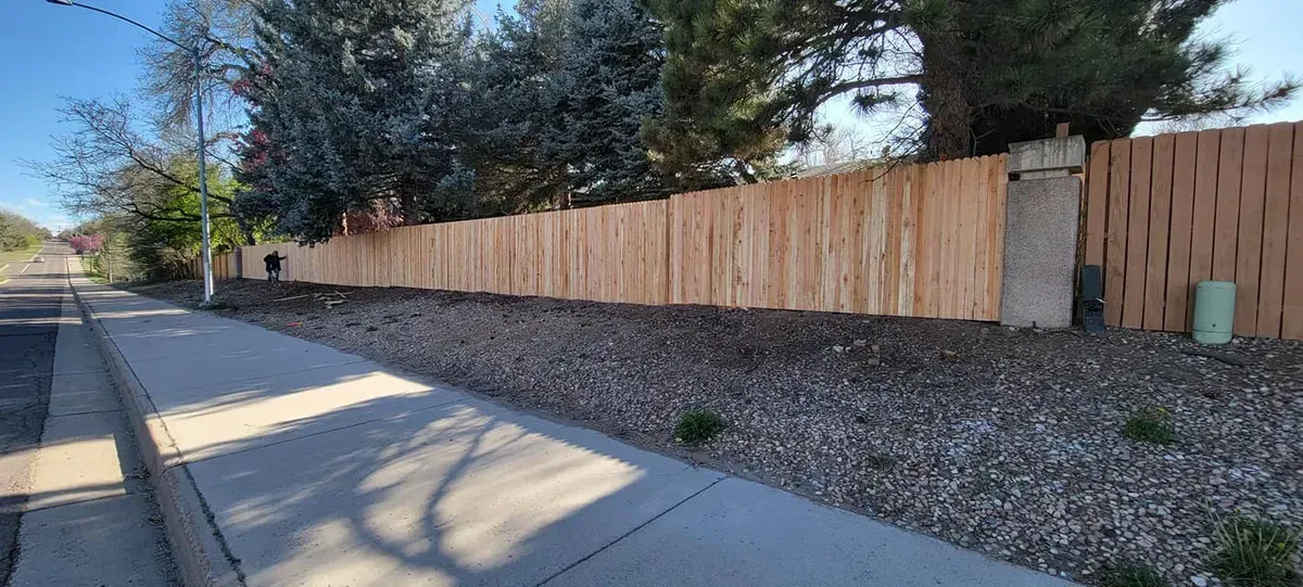 A new wooden fence next to a sidewalk and a gravel bed. 