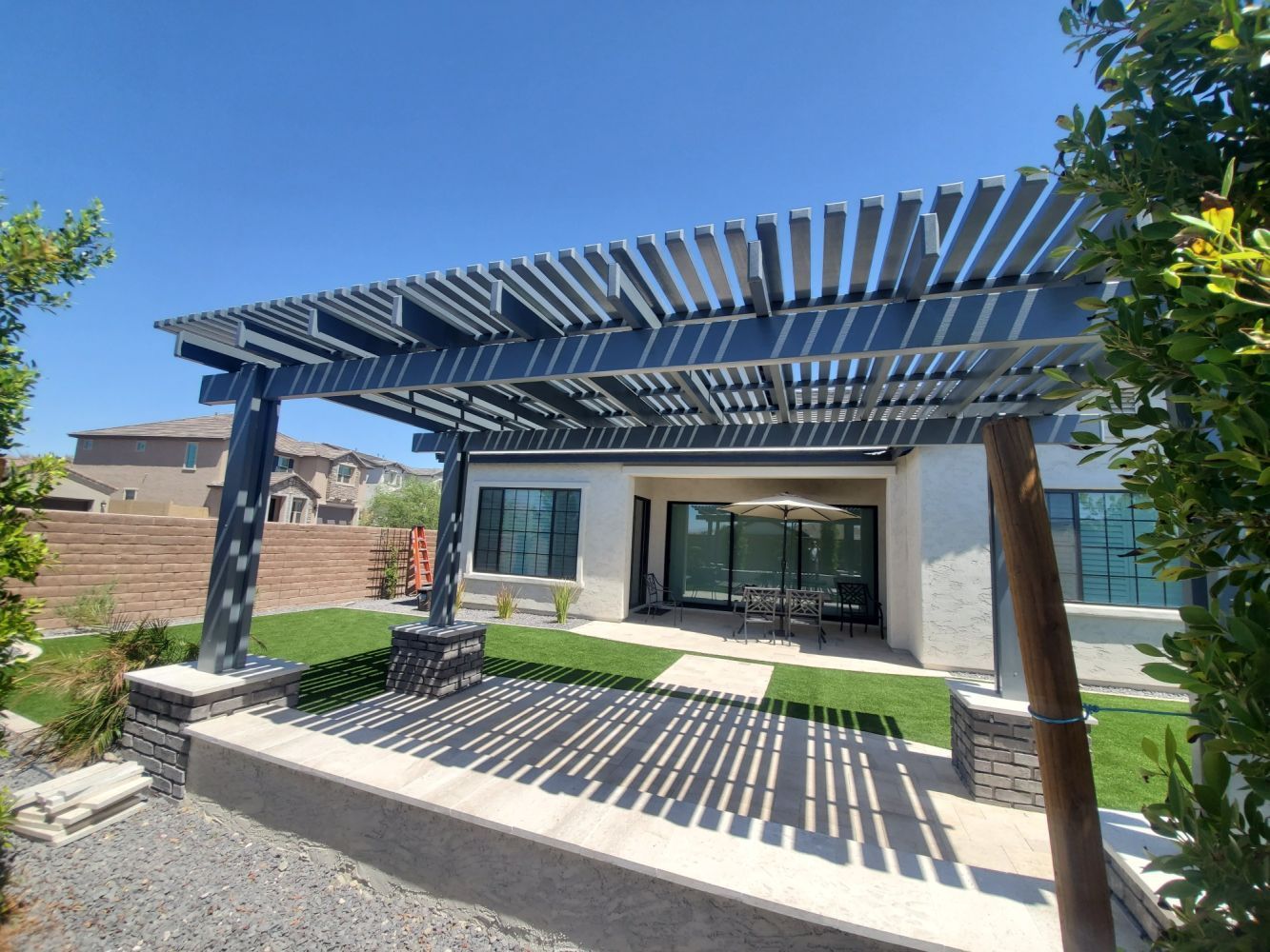 Modern patio pergola with slatted roof casting striped shadows over a paved seating area