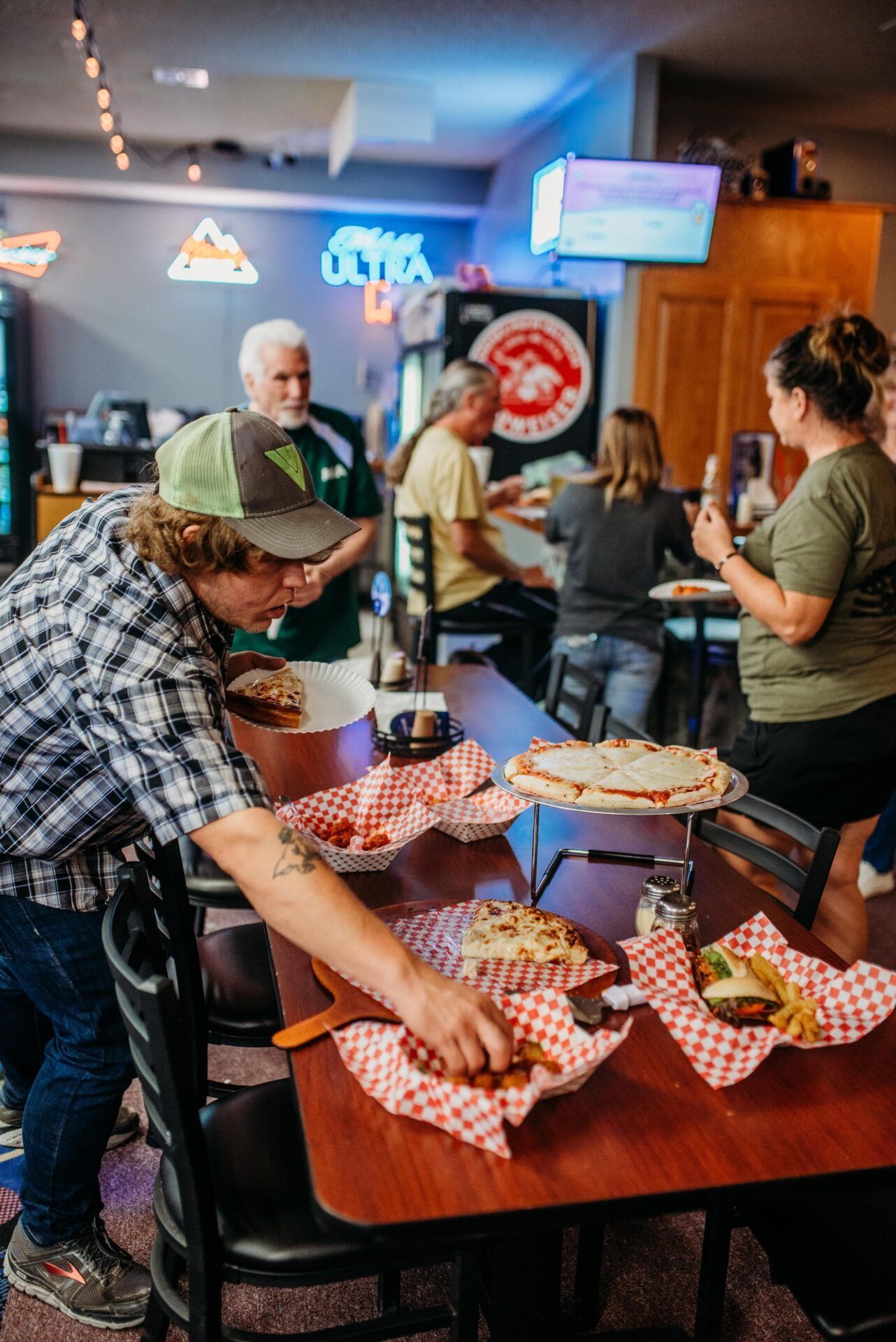 People gathered in a bar around a table with pizza and drinks, chatting in a casual scene.