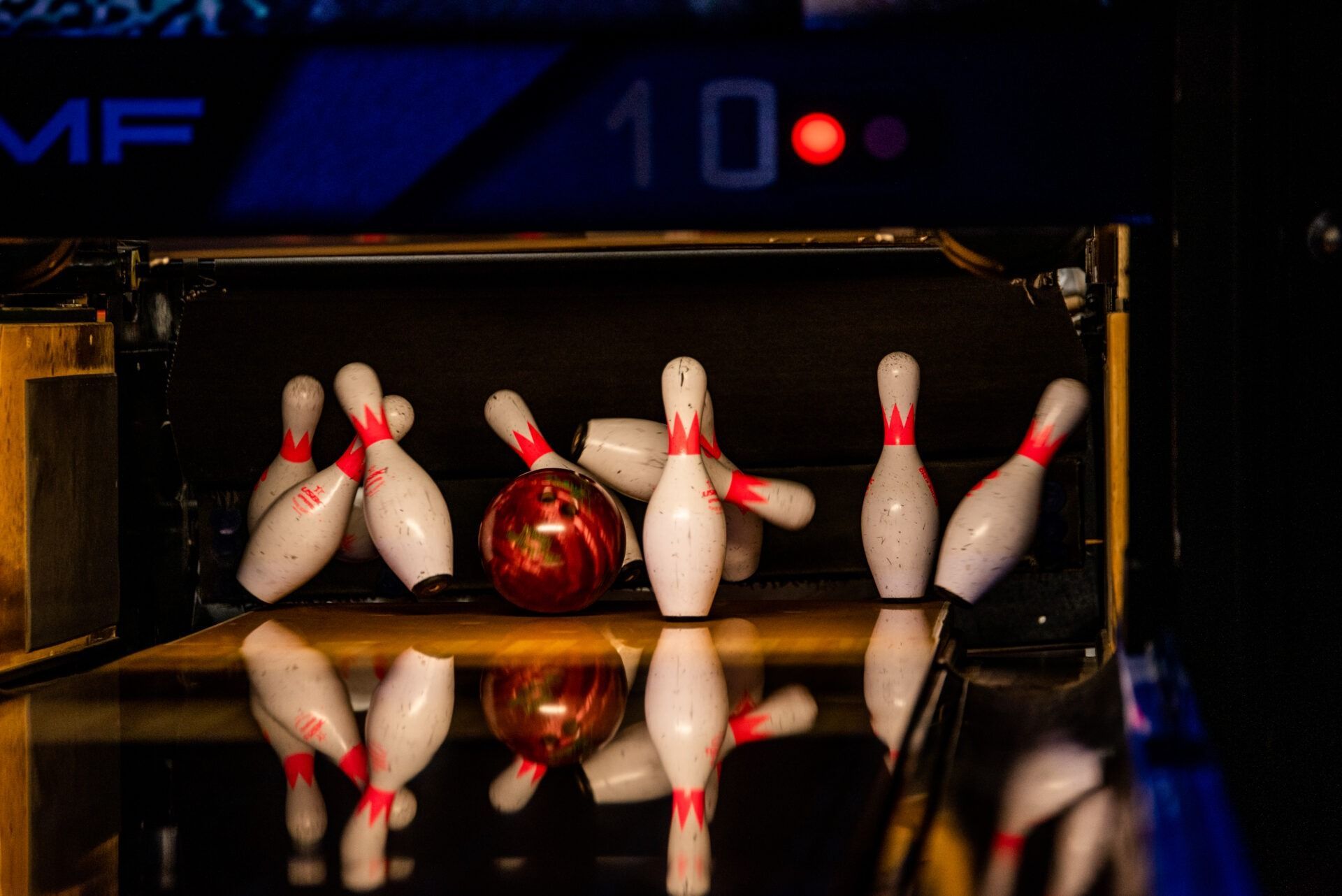 Bowling pins split around a red ball on a glossy lane in a dark bowling alley
