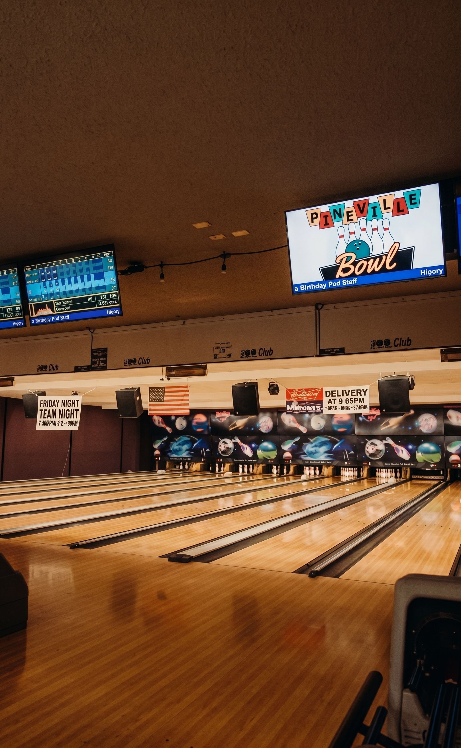 Bowling alley interior with lanes, overhead score screens, and pins set at the far end.