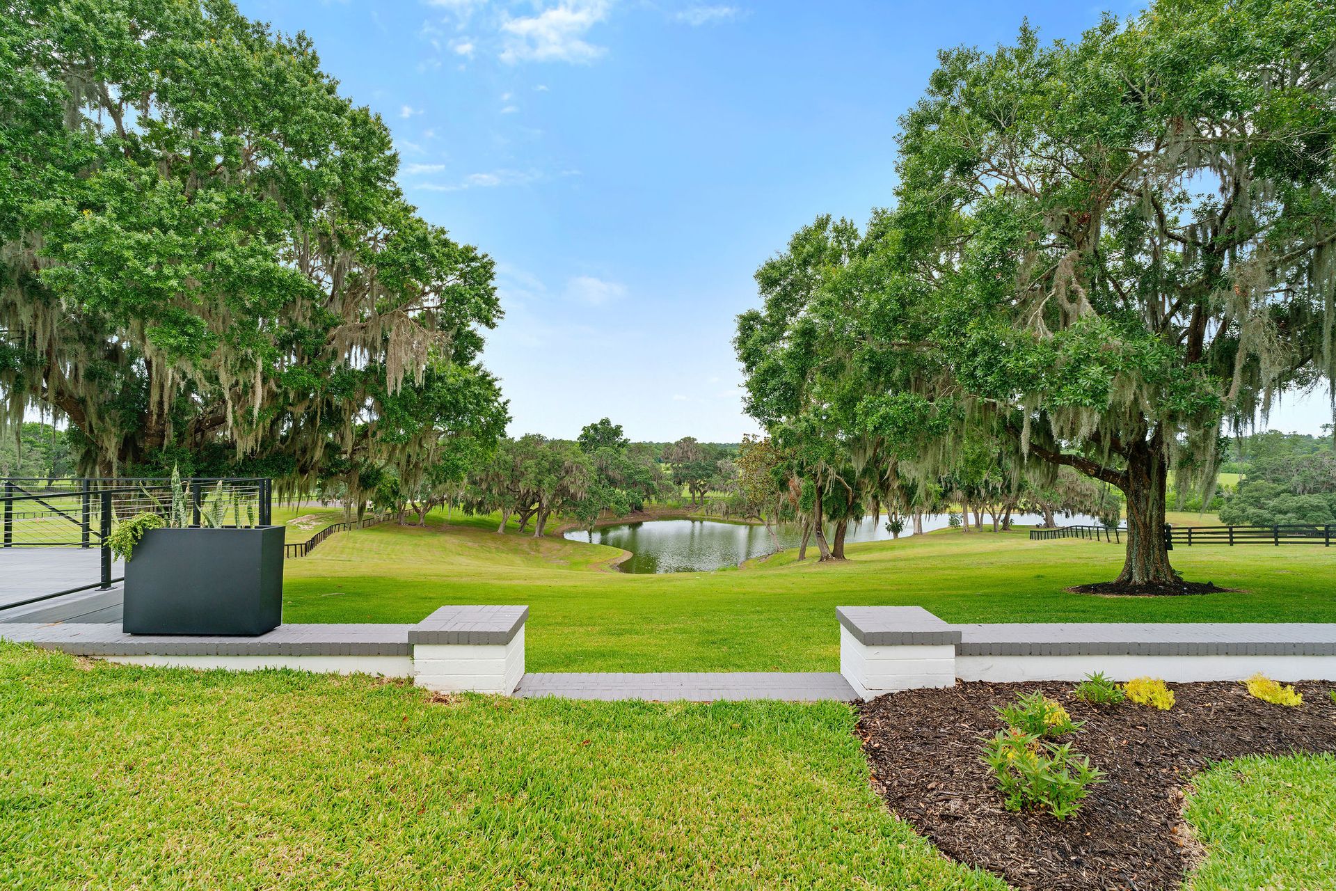 A large lush green field with trees and a pond in the background.