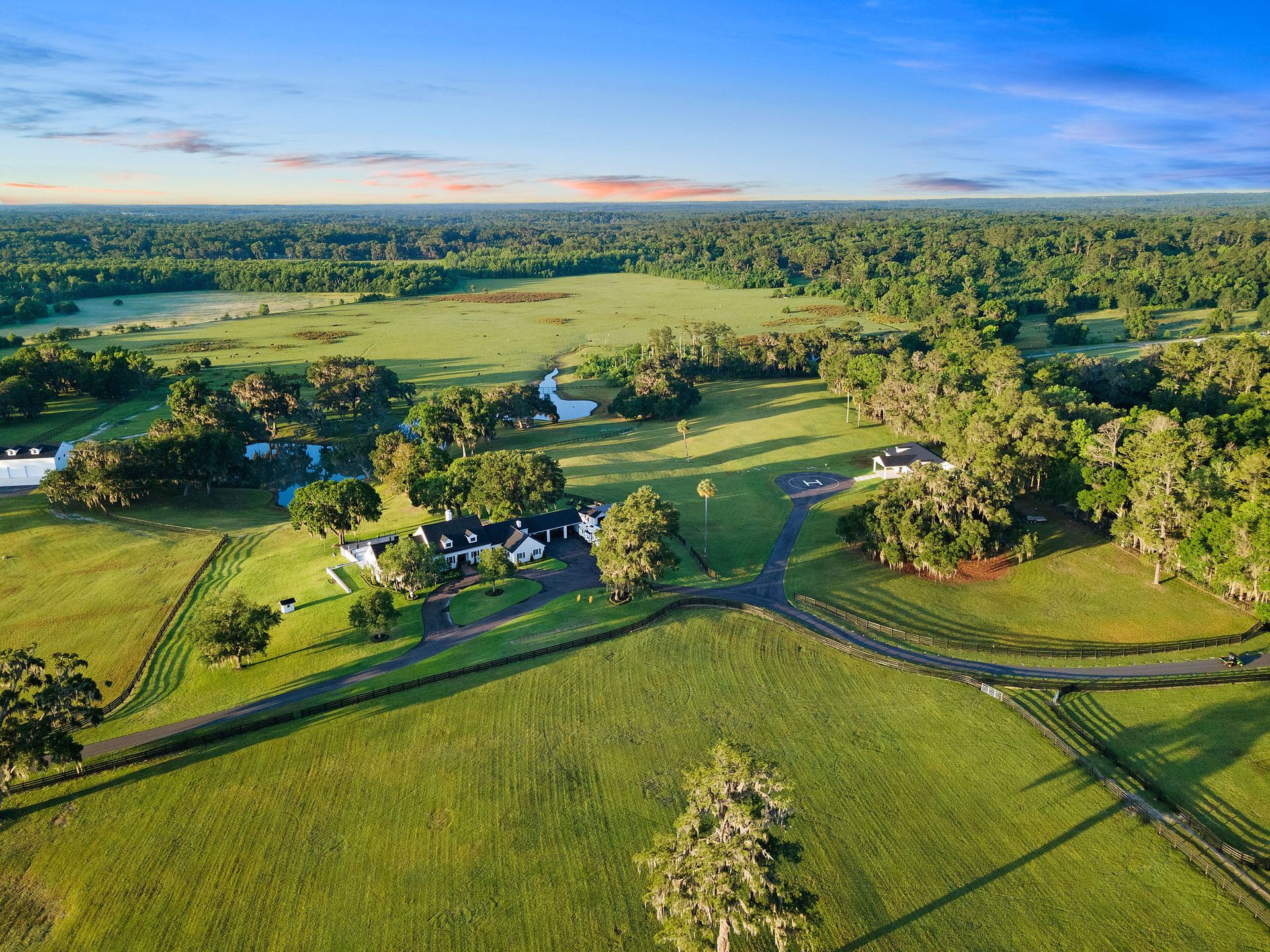 An aerial view of a lush green field with trees and a house in the distance.