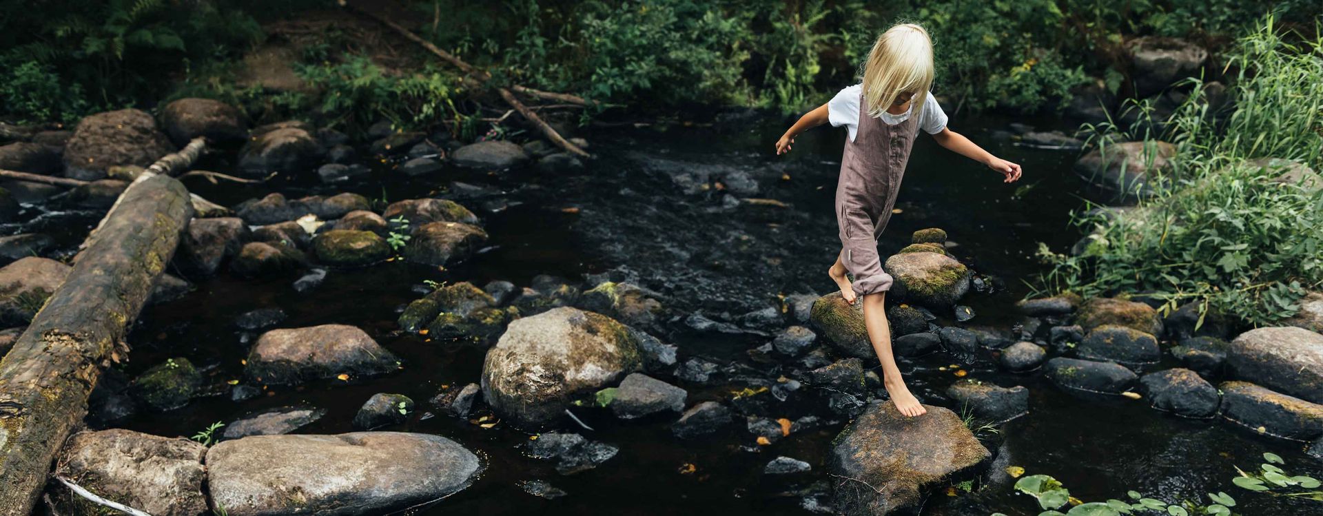Girl crossing over rocks in a clean creek