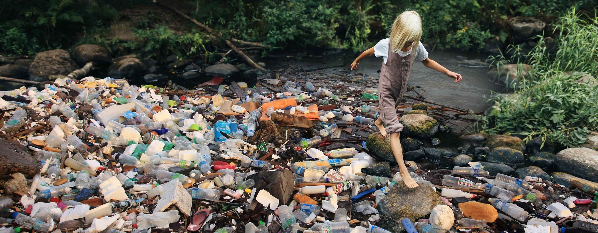 Girl crossing over rocks in a rubbish-polluted creek