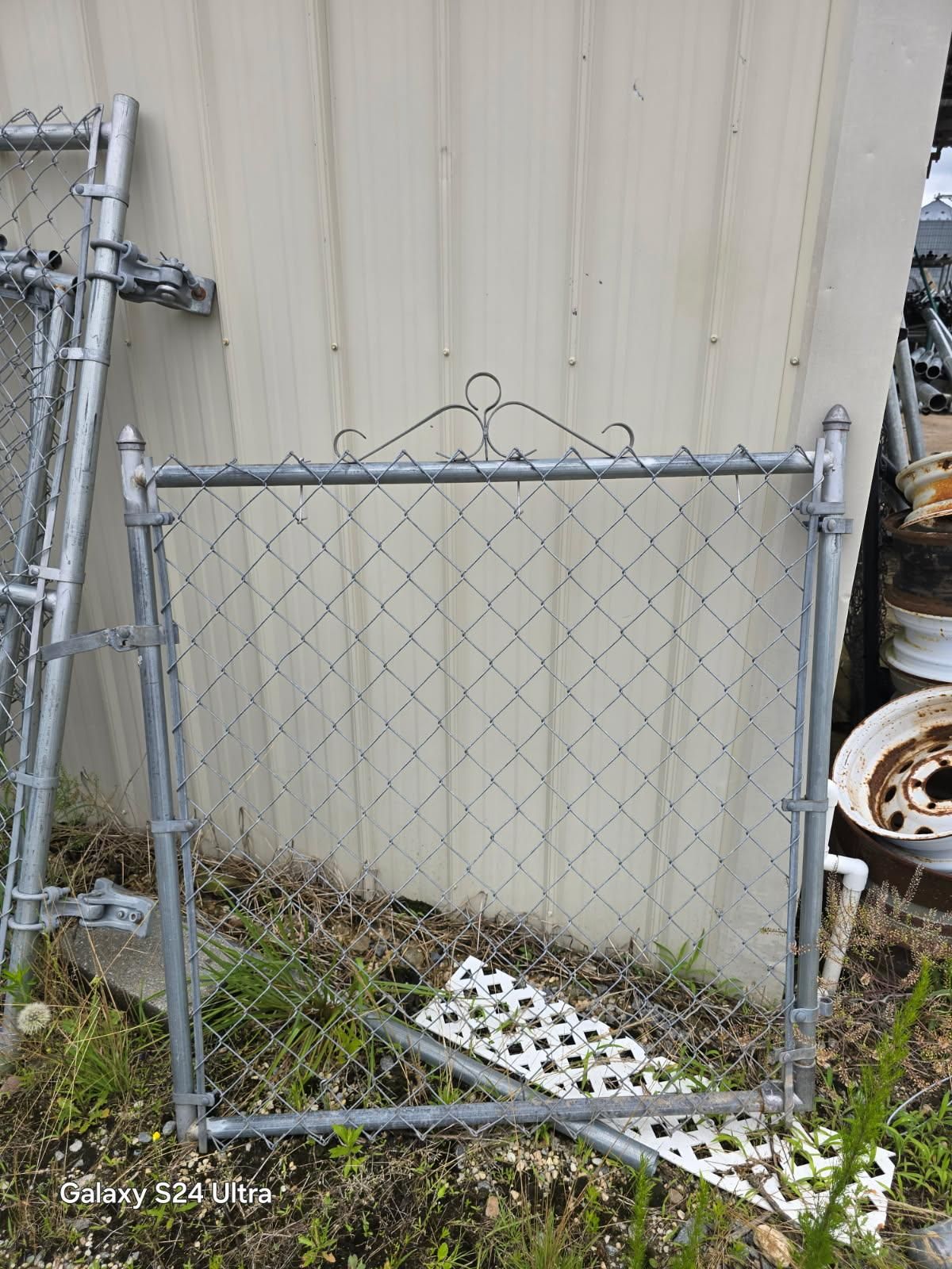 Small chain-link gate leaning against a beige metal wall, with white plastic grates on the ground. Small chain-link gate leaning against a beige metal wall, with white plastic grates on the ground.