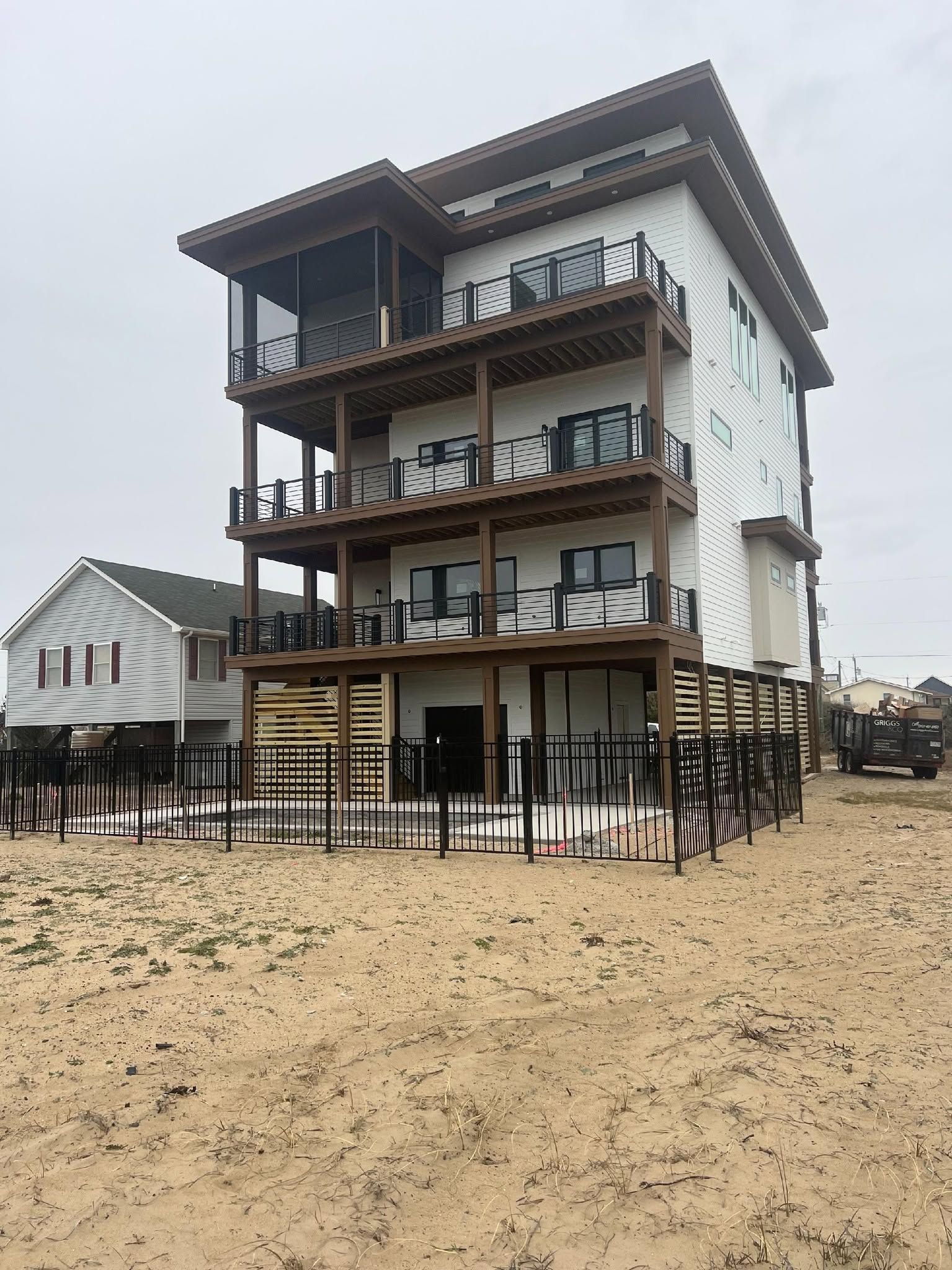 Multi-story beachfront house under construction with wooden balconies and sandy ground under a cloudy sky Multi-story beachfront house under construction with wooden balconies and sandy ground under a cloudy sky