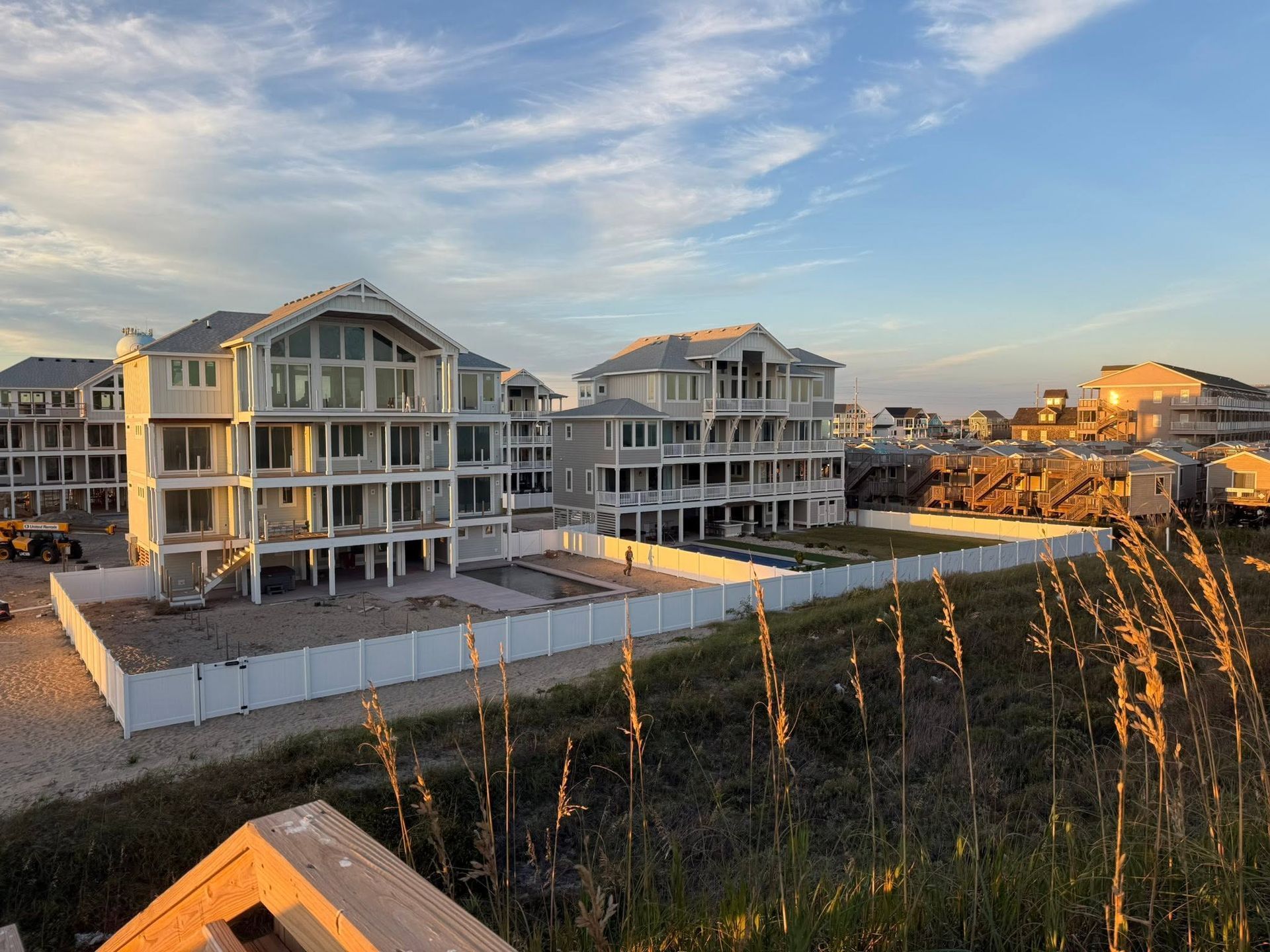 Beachfront houses at sunset with white fences and tall grasses in the foreground