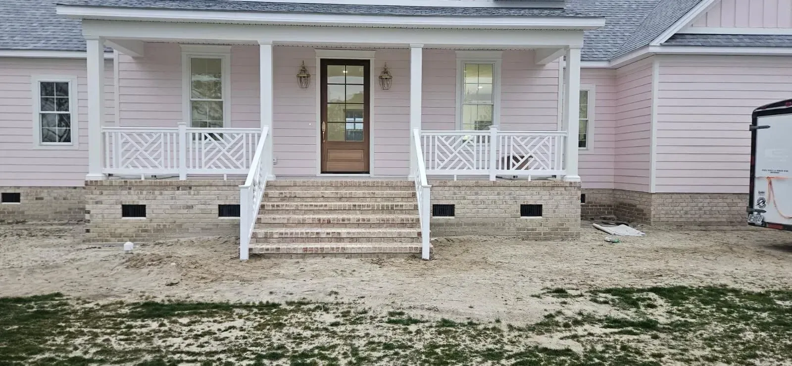 Front porch of a pink house with white railings, steps, and a glass front door on a snowy lawn