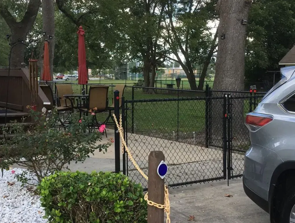Backyard patio with black fence, green chairs, red umbrellas, trees, and parked silver SUV Backyard patio with black fence, green chairs, red umbrellas, trees, and parked silver SUV