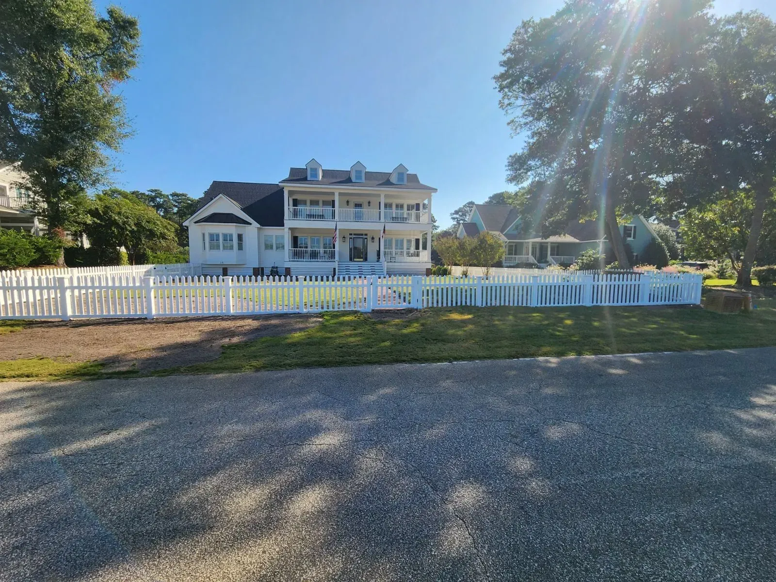 White Victorian-style house with a white picket fence on a sunny tree-lined street