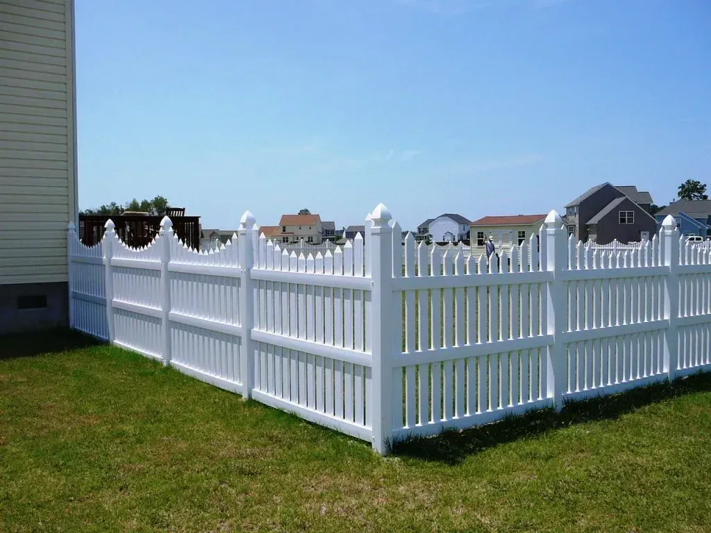 White vinyl fence enclosing a grassy yard with houses in the background under a blue sky