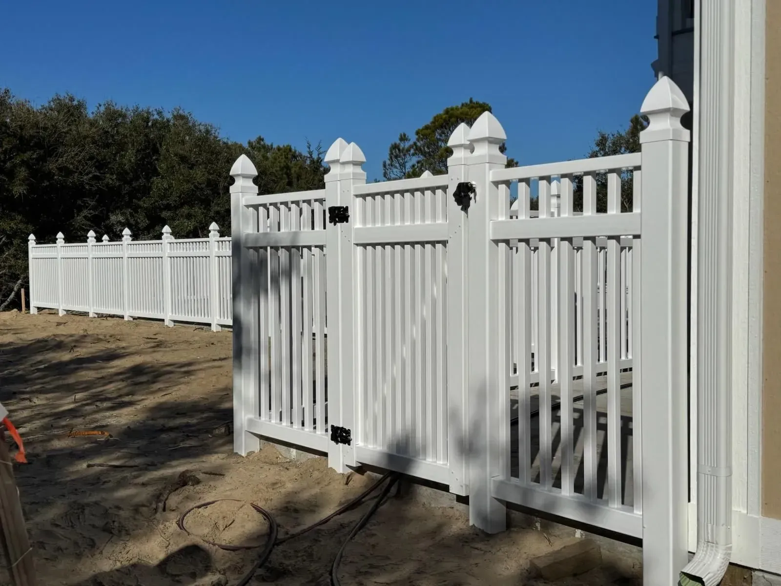 White picket fence and gate along a sandy path under a clear blue sky. White picket fence and gate along a sandy path under a clear blue sky.