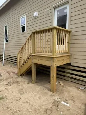 Wooden accessibility ramp and small landing beside a beige house on sandy ground